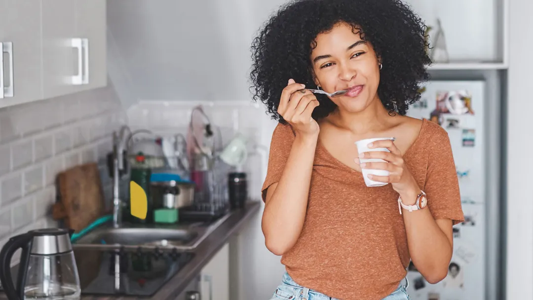 A woman sitting on her counter eating yogurt. 
