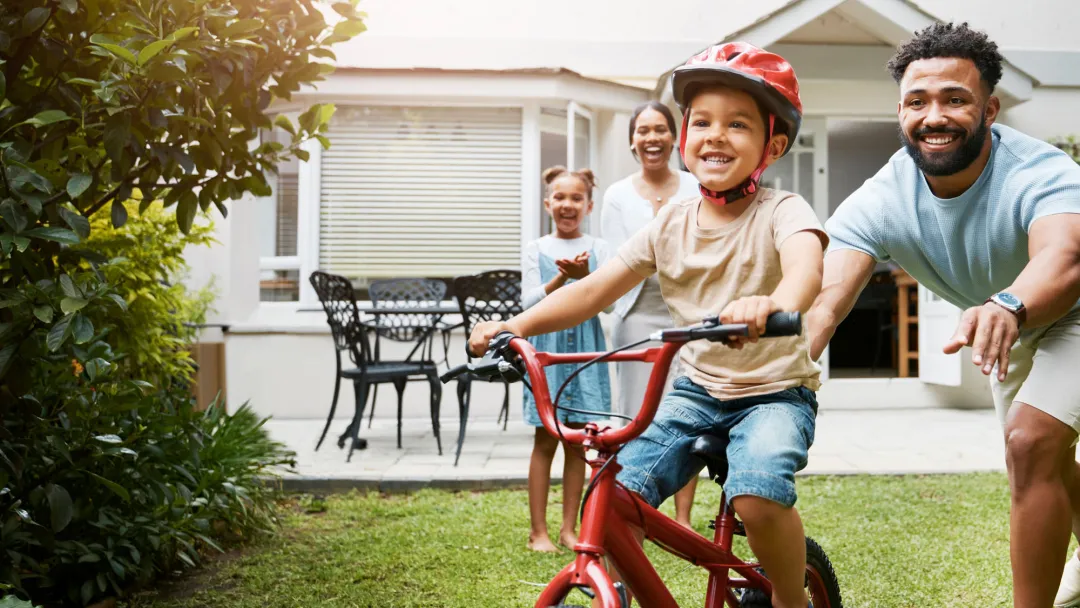 Family teaching son to ride bike in yard.
