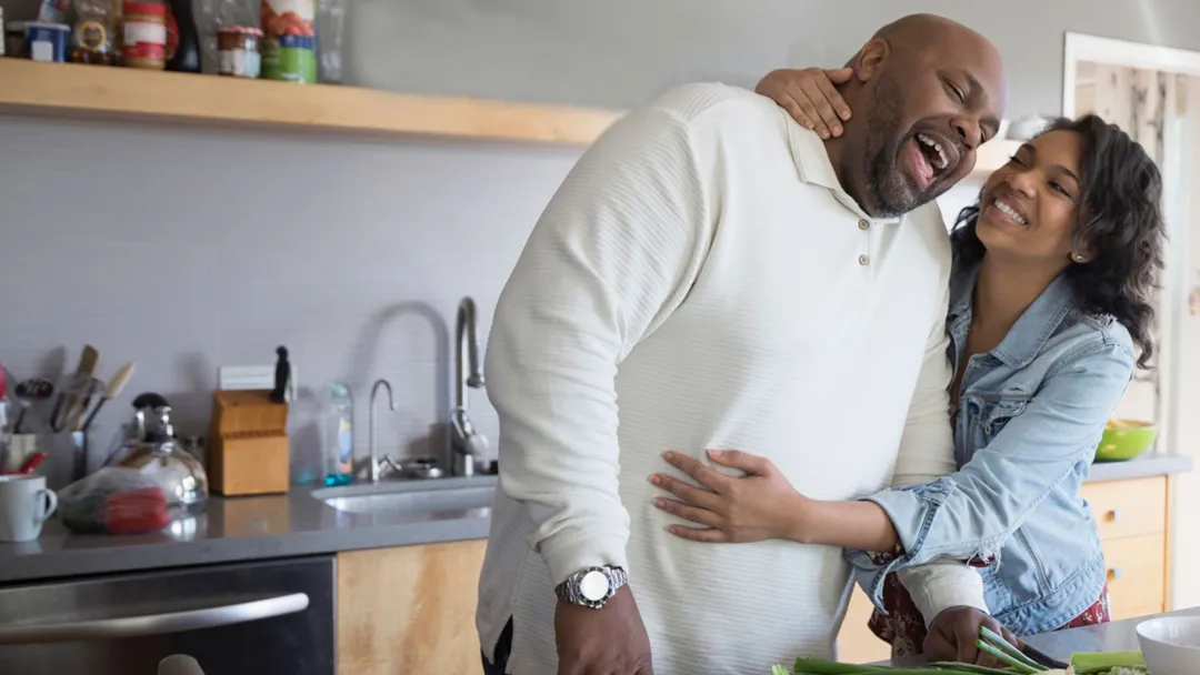 A couple hugging each other while cooking on the kitchen