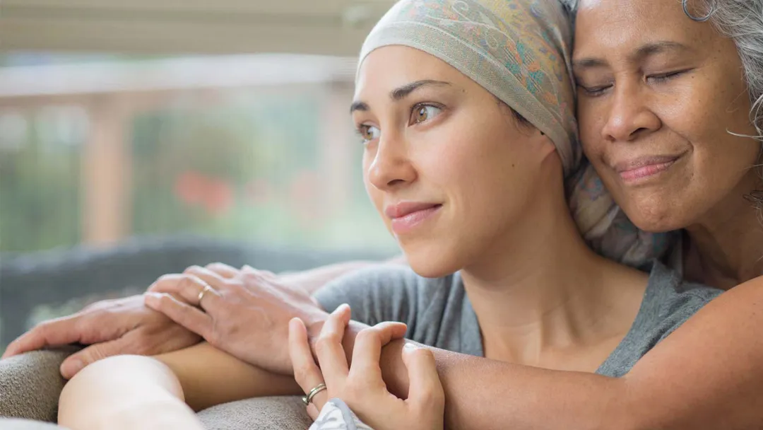 Woman in 50s embracing her mid 30s daughter with Cancer
