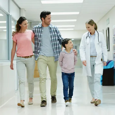 A Smiling Mother, Father and Son Walk Down a Hospital Hallway with a Doctor.