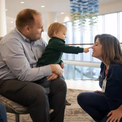 Nurse Smiling at Boy Sitting in Father's Lap Poking Her on the Nose