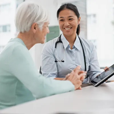 A Physician Smiles While She Goes Over a Patient's Chart With Her on a Tablet.