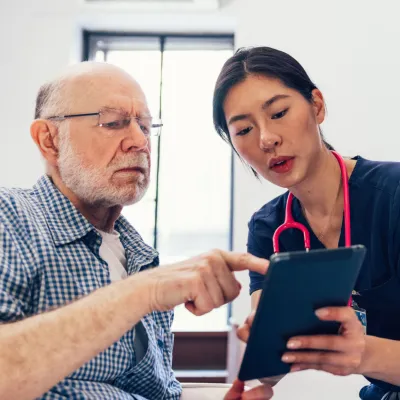 An older man looks at a tablet with a nurse.