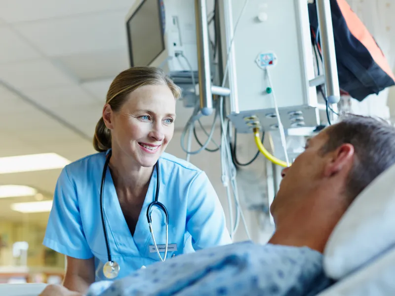 A smiling female physician reassures her male patient in a hospital room.