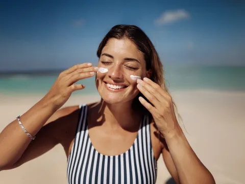 Women applying sunscreen on face at the beach.