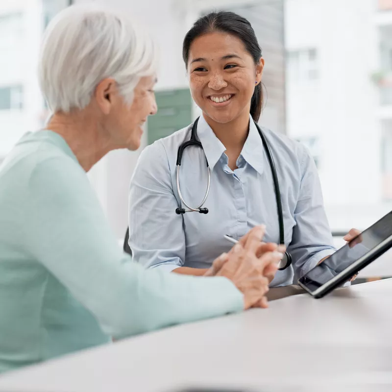 A Physician Smiles While She Goes Over a Patient's Chart With Her on a Tablet.
