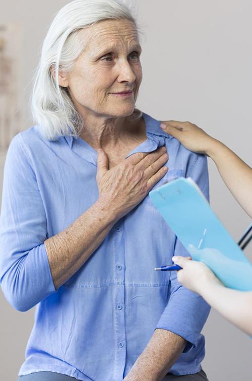 A senior woman clutching her chest, with a tech taking her blood pressure.