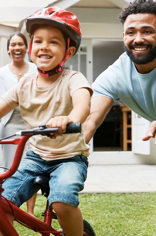 Family teaching son to ride bike in yard.